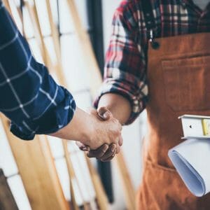 Two people shake hands. One is wearing an industrial apron and holding paperwork
